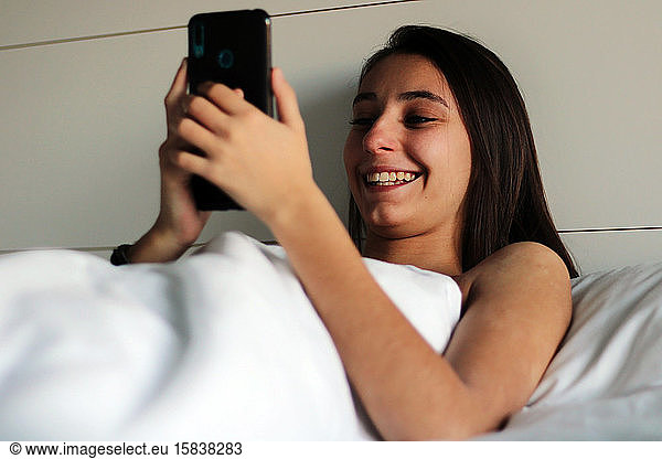 Young and pretty girl just woke up using the cell phone in bed.