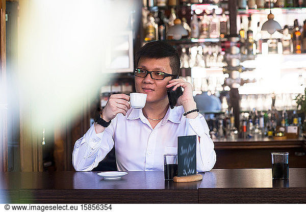 young asia man in a bar with a cup of coffee and smart phone