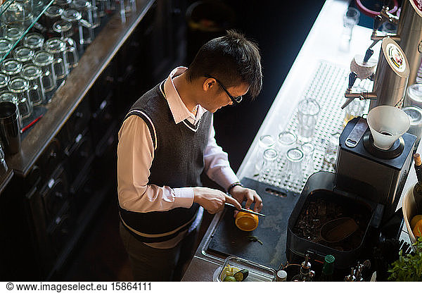 young asia waiter in a bar cutting an orange