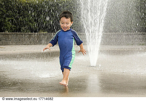 Young Asian-Caucasian Boy Playing In A Water Sprinkler; Ontario Canada