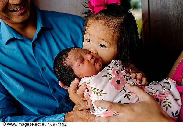 Young asian girl kisses cheek of brand new baby sister