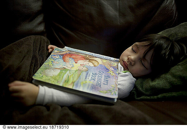 Young Asian girl sleeps with book resting on her.