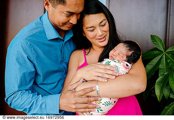 Young asian parents lovingly hold sleeping newborn daughter