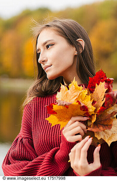 Young asian woman in red jumper holding yellow maple leaves