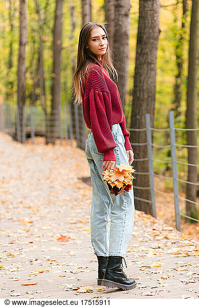 Young asian woman in red jumper holding yellow maple leaves in park