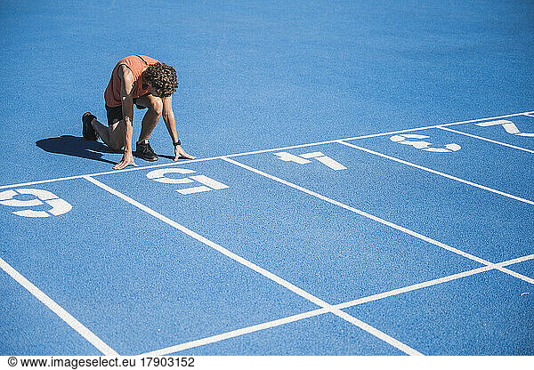 Young athlete kneeling at starting line on sunny day
