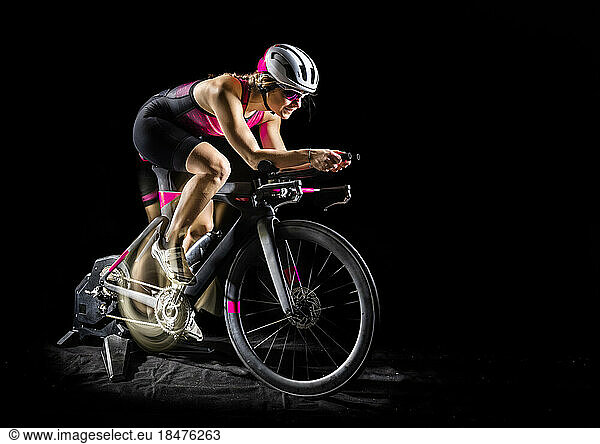 Young athlete sitting on turbo bike against black background