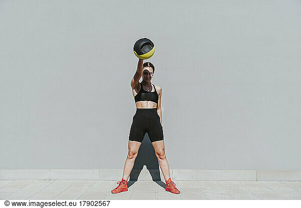 Young athlete with medicine ball exercising in front of gray wall
