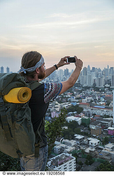 Young backpacker photographing city with smart phone at sunset