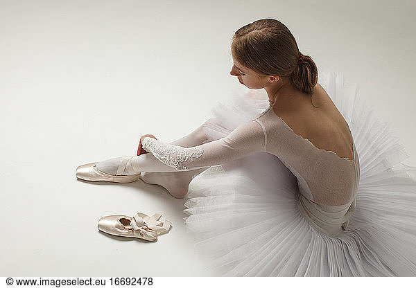 young ballerina in white ballet dress Putting On Ballet Shoes  sitting