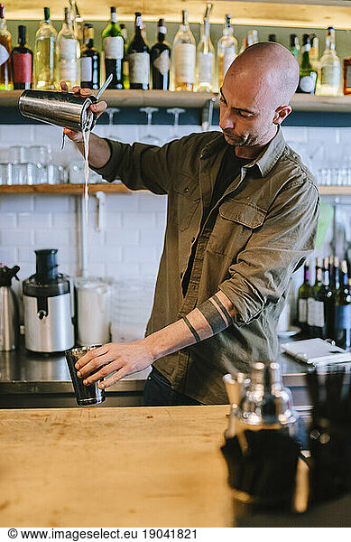 Young barman prepares an alcoholic cocktail in the bar