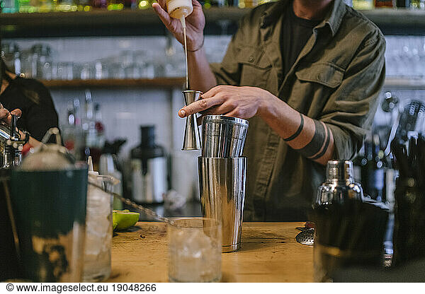 Young barman prepares an alcoholic cocktail in the bar