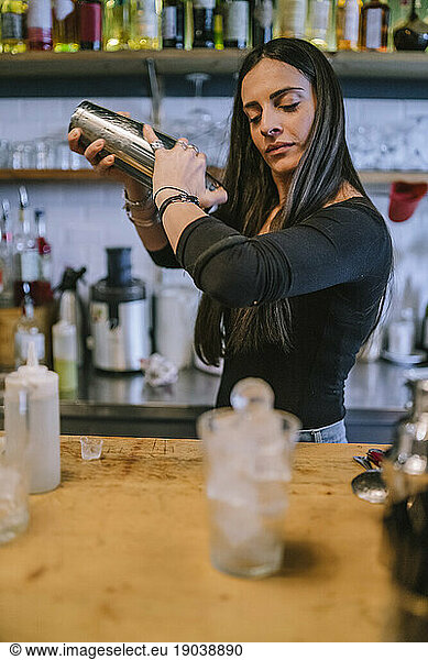 Young barwoman prepares an alcoholic cocktail in the bar