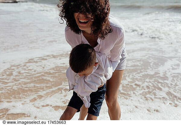 Young beautiful mommy playing with her baby son on the beach