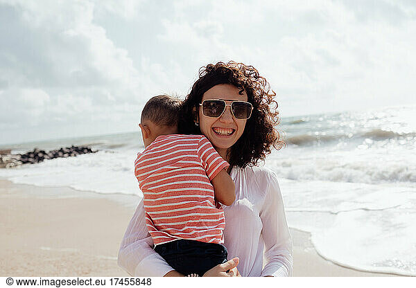 Young beautiful mommy playing with her baby son on the beach