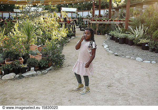 Young black girl with long hair near among plants at nursery