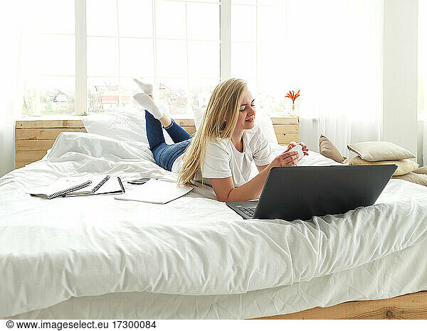 young blond female opening the headphones box lying on white bed