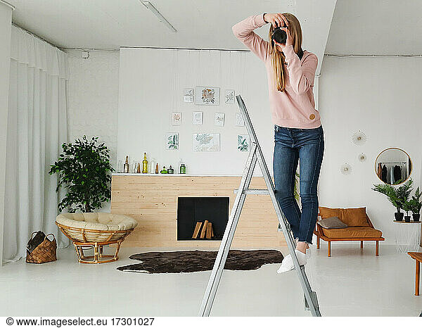 young blond female photographer making photo on the step-ladder