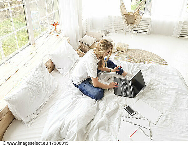 young blond female sitting with laptop in bed