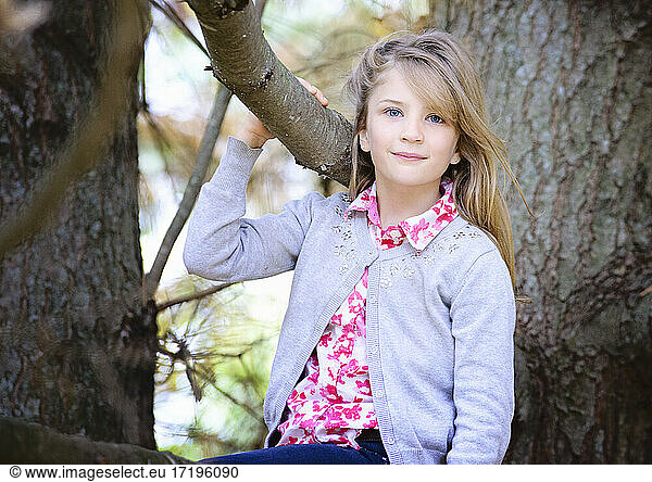 Young blond girl outside sitting in a tree.