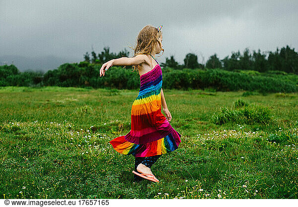 Young blond girl twirls in green grassy plain in rainbow dress