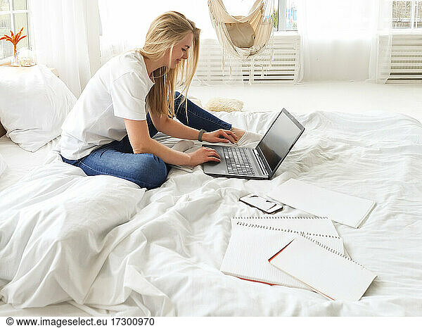 young blond-hair female working on the laptop in white bed