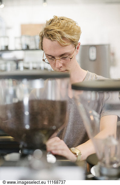 Young blond man with spectacles standing at an espresso machine in a coffee shop.