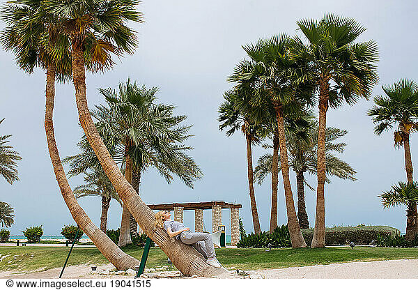 Young blond woman laying on palm tree