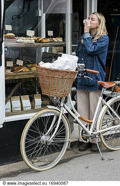 Young blond woman standing next to bicycle outside waste free wholefood store.