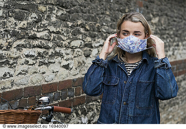 Young blond woman standing outdoors  putting on face mask.