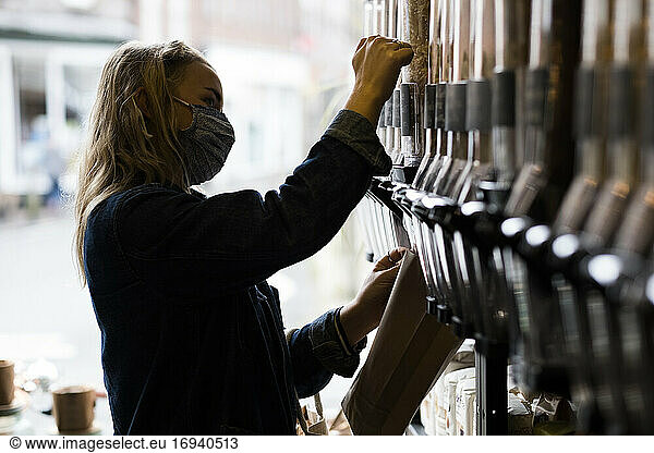 Young blond woman wearing face mask  shopping in waste free wholefood store.