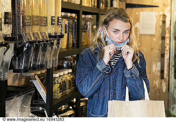 Young blond woman wearing face mask  shopping in waste free wholefood store.