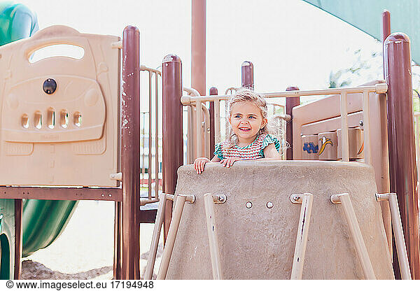 Young blonde girl playing at a public playground on a sunny day.