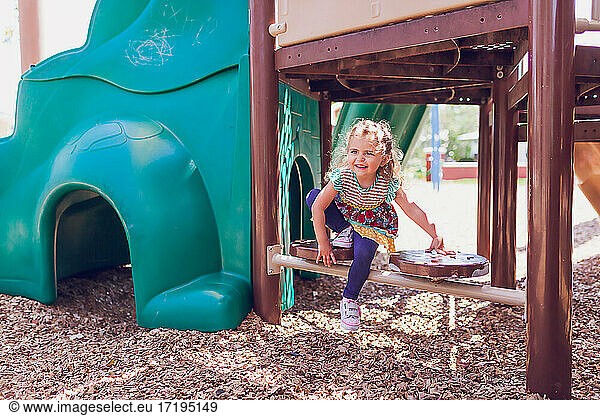 Young blonde girl playing at a public playground on a sunny day.