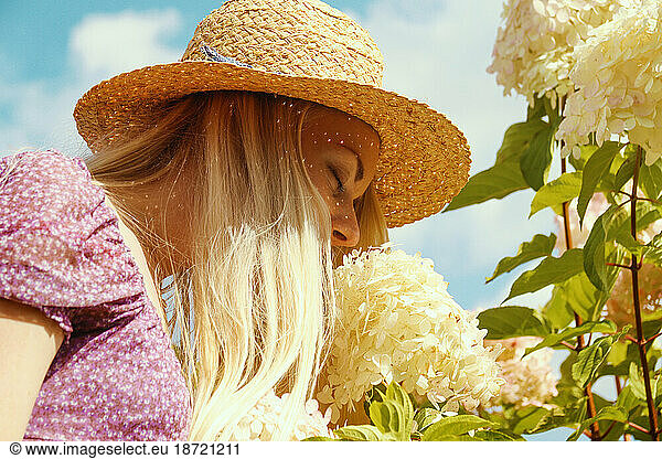 Young blonde woman in a straw hat smell the flowers