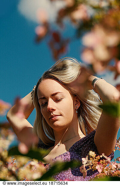 Young blonde woman plays with her hair surrounded by pink flowers