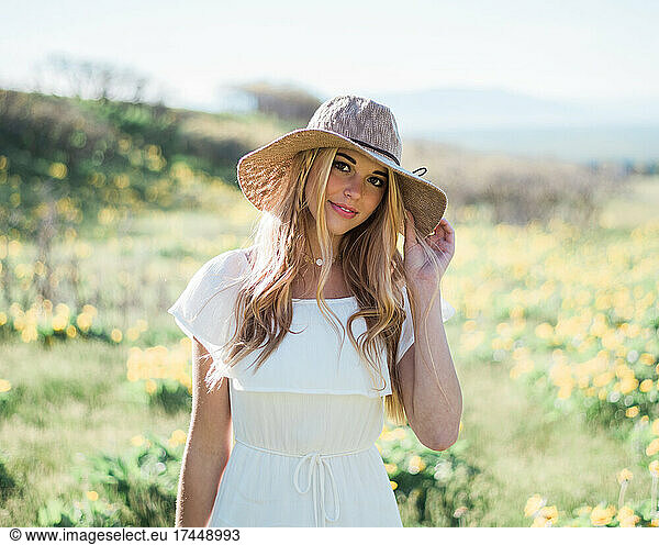 Young Blonde Woman with Summer Beach Hat in Field of Flowers