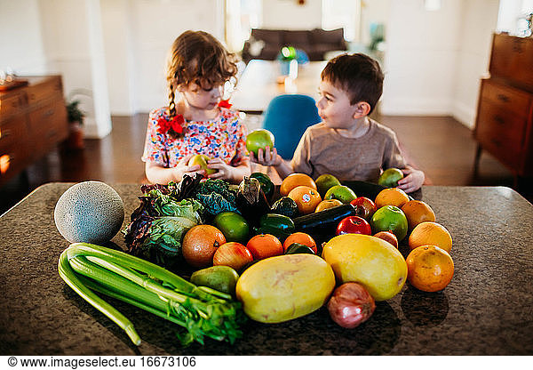 Young boy and girl sitting in kitchen with counter full of fruit