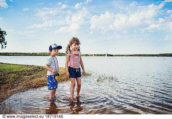 Young boy and girl standing in water at lake wearing binoculars