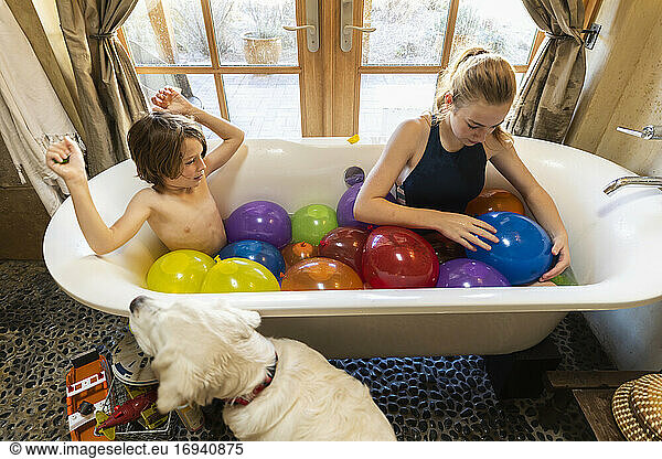 Young boy and his older sister in bathtub filled with water balloons