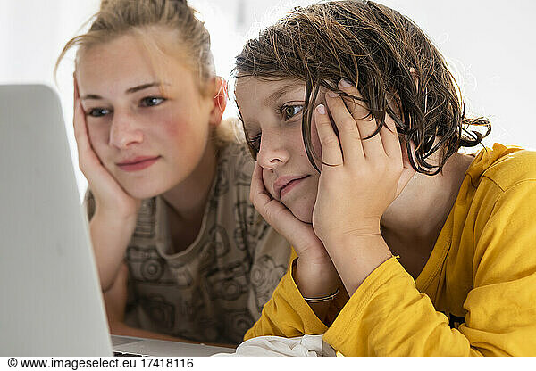 Young boy and teenage sister sharing a laptop  watching in a bedroom