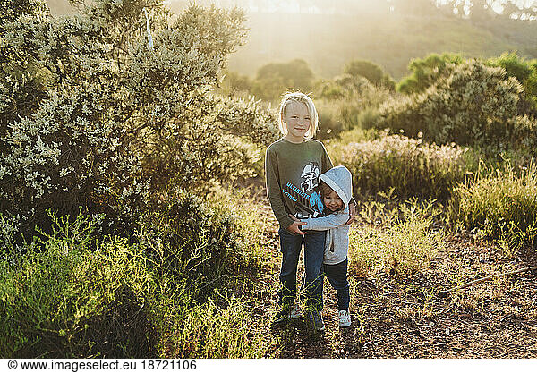 Young boy and toddler sister hugging in backlit field
