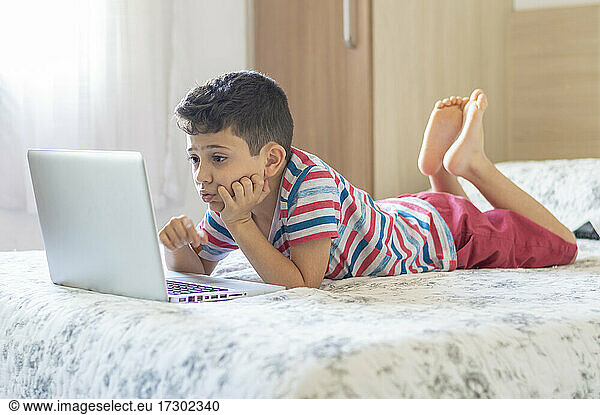 Young boy child lying on bed using a laptop. Online class lesson