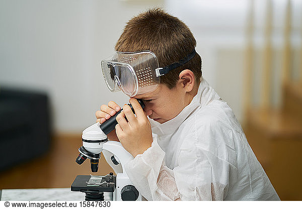 young boy dressed in a white robe and protective goggles observes thro