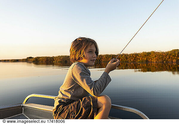 Young boy fishing from a boat on the Okavango Delta at sunset  Botswana.
