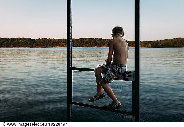 Young boy fishing in lake off dock at sunset