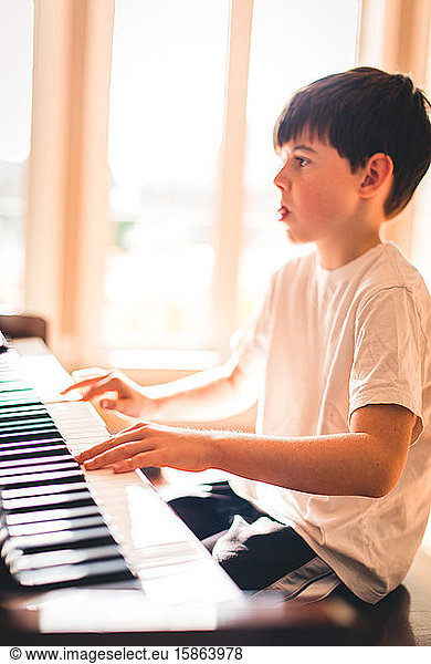 Young boy focused while playing the piano in a sunny room.