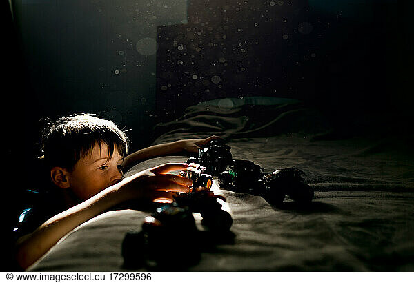 Young boy in blue shirt playing with cars on a bed in bedroom