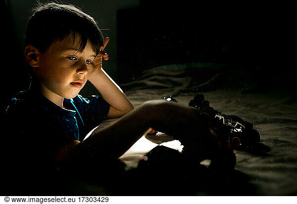 Young boy in blue shirt playing with cars on a bed in bedroom