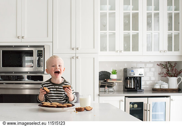 Young boy in kitchen  holding freshly baked cakes  smiling